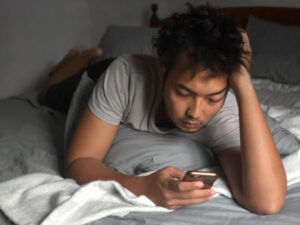Man laying on bed using social media on his phone