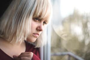 Close up of depressed young blond woman near window at home. 